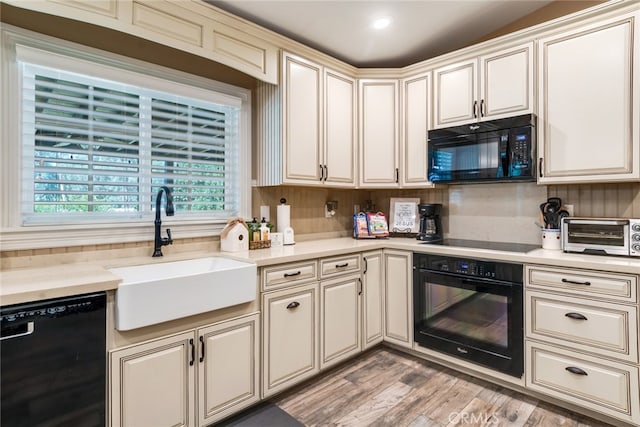 kitchen with sink, light hardwood / wood-style flooring, black appliances, backsplash, and cream cabinets