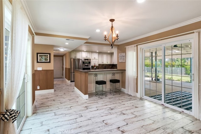 kitchen with appliances with stainless steel finishes, backsplash, kitchen peninsula, an inviting chandelier, and ornamental molding