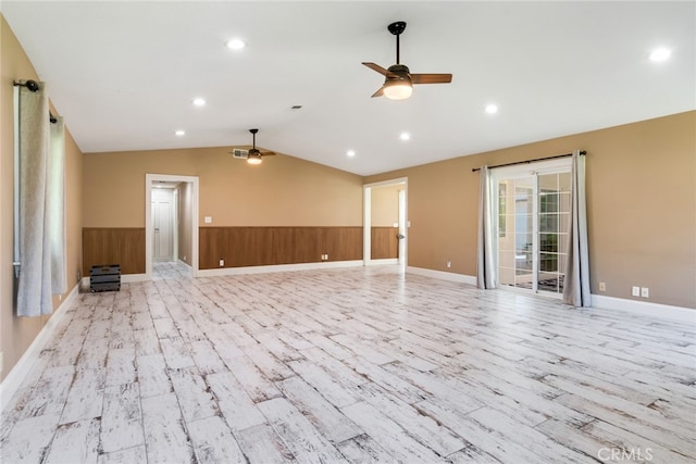 unfurnished living room featuring ceiling fan, vaulted ceiling, wood walls, and light hardwood / wood-style floors