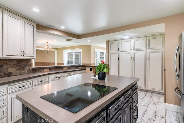 kitchen featuring stainless steel refrigerator, backsplash, a center island, black electric stovetop, and a notable chandelier