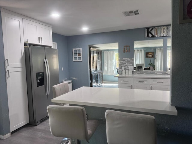 kitchen featuring stainless steel fridge with ice dispenser, white cabinetry, and a kitchen breakfast bar