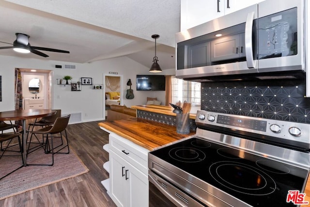 kitchen featuring dark wood-type flooring, vaulted ceiling, decorative backsplash, appliances with stainless steel finishes, and decorative light fixtures