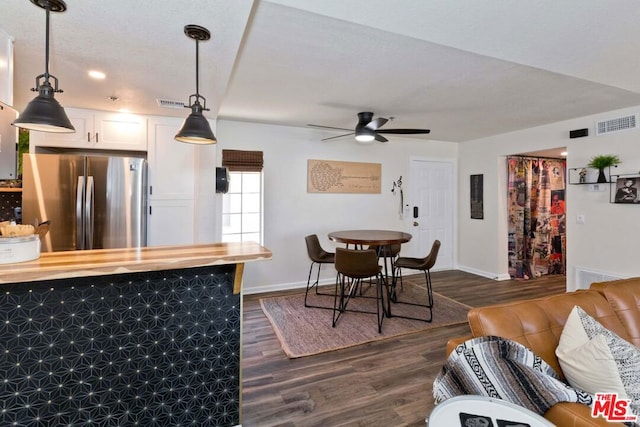 kitchen featuring white cabinets, stainless steel refrigerator, hanging light fixtures, and dark wood-type flooring