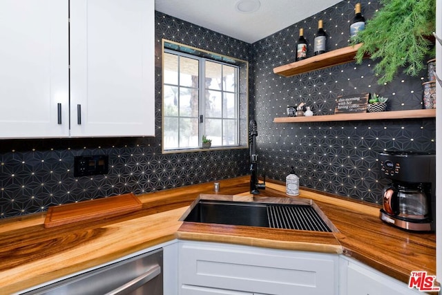 kitchen featuring wood counters, dishwasher, white cabinets, sink, and tasteful backsplash