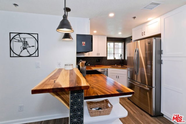 kitchen with white cabinets, kitchen peninsula, appliances with stainless steel finishes, decorative light fixtures, and butcher block counters