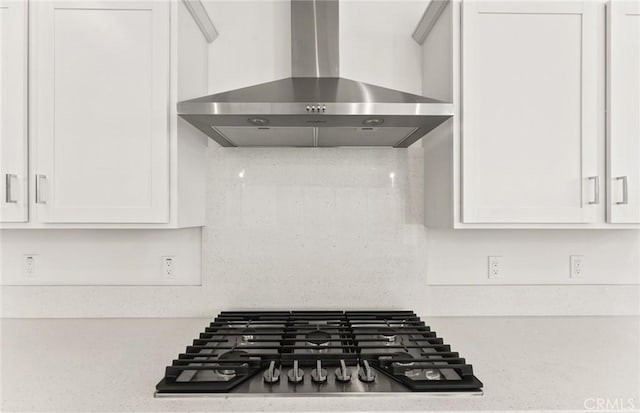 details with white cabinetry, stainless steel gas cooktop, wall chimney range hood, and tasteful backsplash