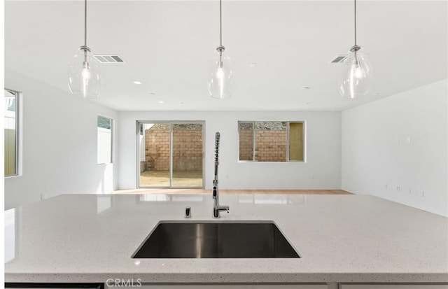 kitchen featuring sink, light stone counters, and pendant lighting