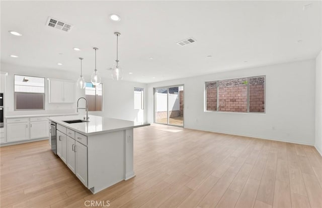 kitchen with sink, white cabinetry, stainless steel appliances, hanging light fixtures, and a kitchen island with sink