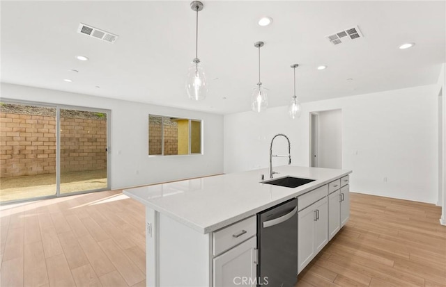 kitchen with an island with sink, hanging light fixtures, sink, stainless steel dishwasher, and white cabinets