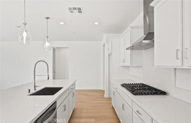 kitchen with appliances with stainless steel finishes, wall chimney exhaust hood, white cabinets, pendant lighting, and sink