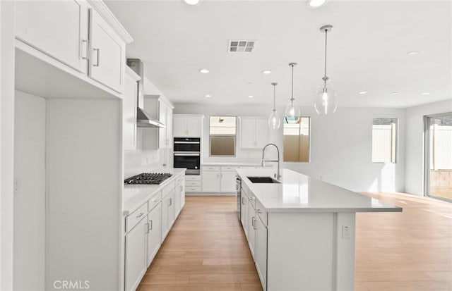 kitchen featuring a center island with sink, sink, white cabinetry, pendant lighting, and wall chimney exhaust hood