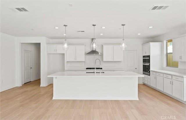 kitchen with an island with sink, wall chimney exhaust hood, and pendant lighting