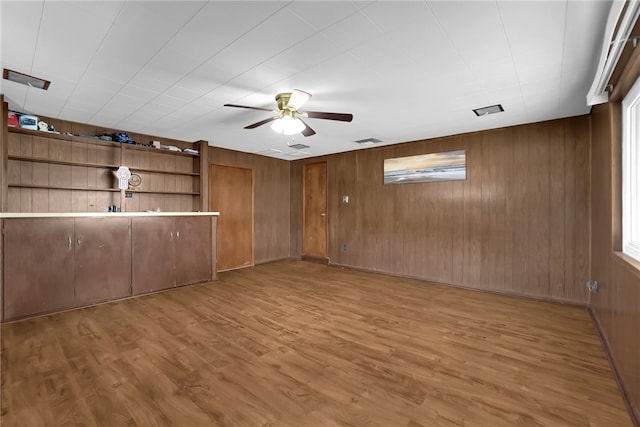 empty room with visible vents, wooden walls, a ceiling fan, and wood finished floors