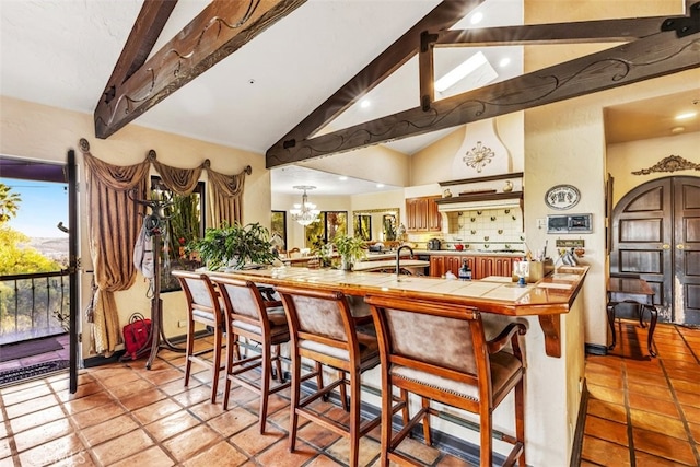 kitchen with decorative backsplash, kitchen peninsula, lofted ceiling with beams, a chandelier, and a breakfast bar