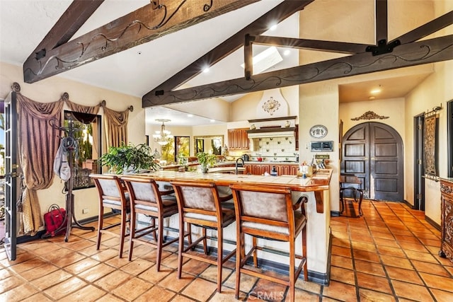 kitchen with beamed ceiling, an inviting chandelier, a kitchen breakfast bar, kitchen peninsula, and light tile patterned floors