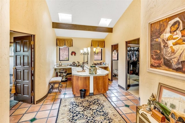 kitchen featuring kitchen peninsula, light tile patterned floors, vaulted ceiling with skylight, and sink