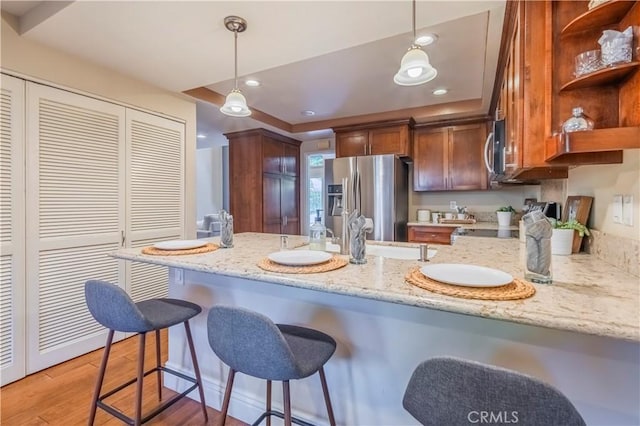 kitchen featuring light stone countertops, kitchen peninsula, light hardwood / wood-style floors, decorative light fixtures, and appliances with stainless steel finishes