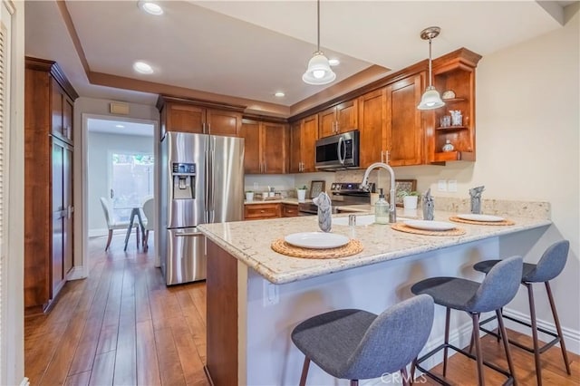 kitchen featuring kitchen peninsula, appliances with stainless steel finishes, pendant lighting, hardwood / wood-style flooring, and a breakfast bar area