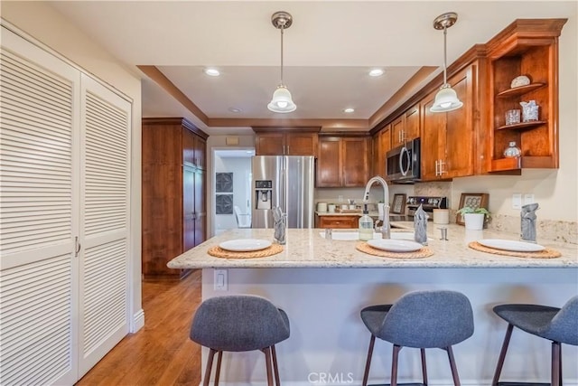 kitchen with kitchen peninsula, decorative light fixtures, stainless steel appliances, and hardwood / wood-style flooring