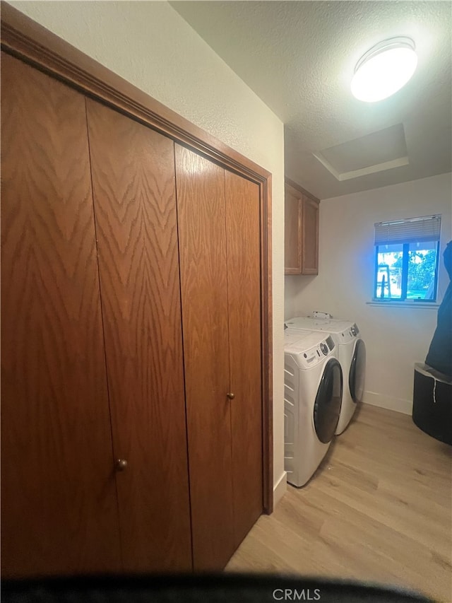 washroom featuring cabinets, light hardwood / wood-style floors, washer and clothes dryer, and a textured ceiling