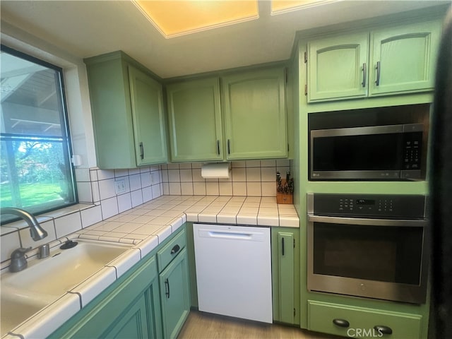 kitchen with appliances with stainless steel finishes, tile countertops, green cabinets, and decorative backsplash