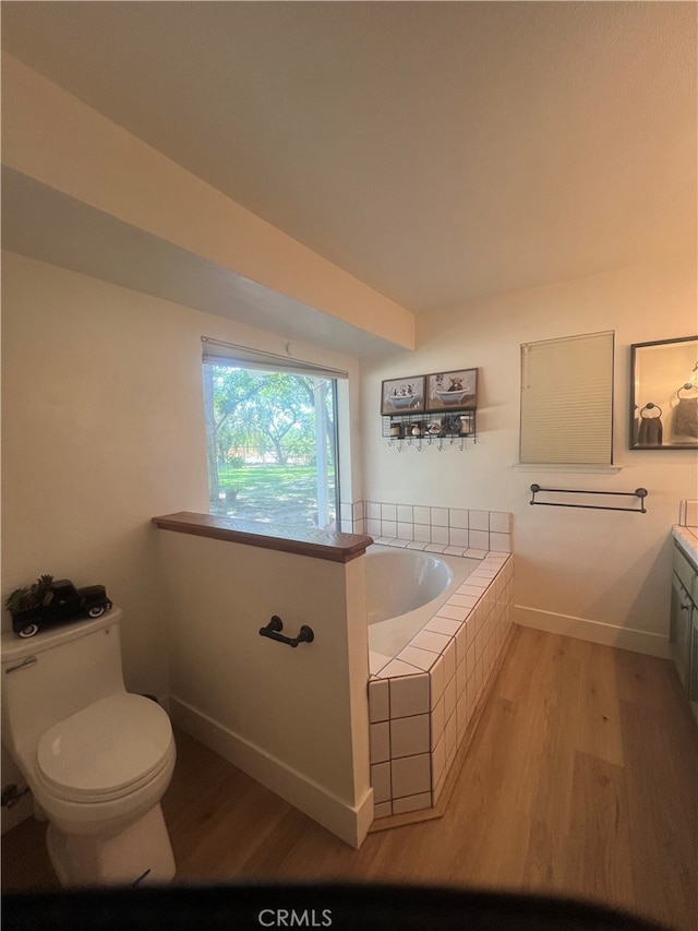 bathroom featuring toilet, tiled tub, vanity, and hardwood / wood-style floors