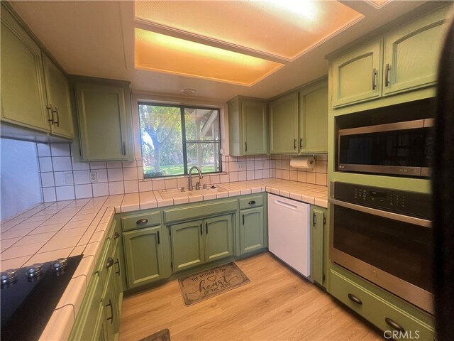 kitchen with backsplash, tile countertops, stainless steel appliances, green cabinets, and light hardwood / wood-style floors