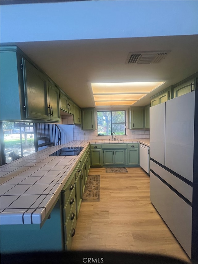 kitchen with light hardwood / wood-style floors, tasteful backsplash, green cabinetry, white appliances, and tile countertops