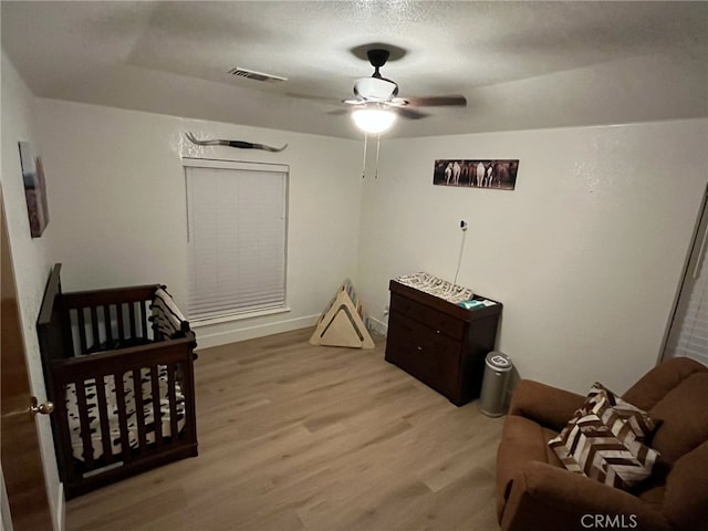 bedroom with ceiling fan, a nursery area, and light hardwood / wood-style floors