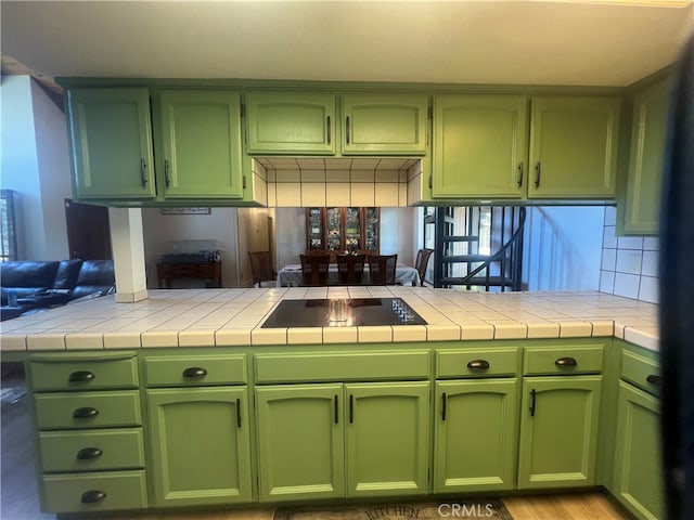 kitchen with tile counters, tasteful backsplash, kitchen peninsula, green cabinets, and black electric cooktop