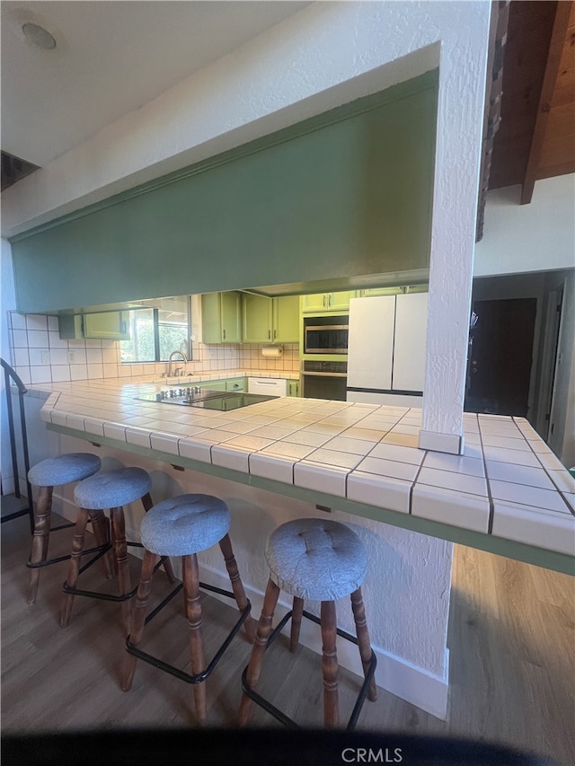 kitchen featuring decorative backsplash, a kitchen bar, light hardwood / wood-style flooring, and tile countertops