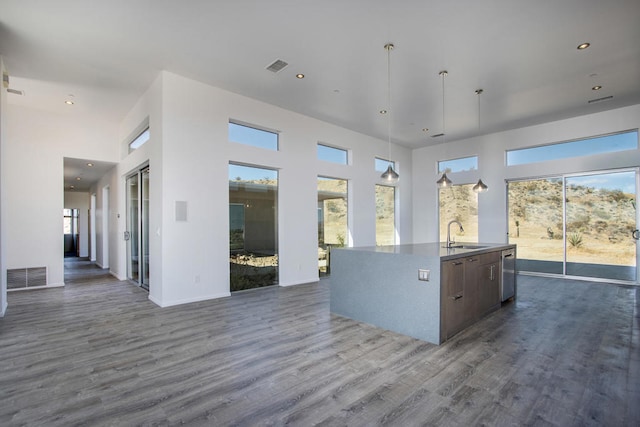 kitchen with a towering ceiling, pendant lighting, a healthy amount of sunlight, a kitchen island with sink, and sink