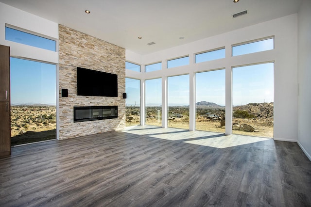 unfurnished living room with a stone fireplace, dark hardwood / wood-style floors, and a high ceiling