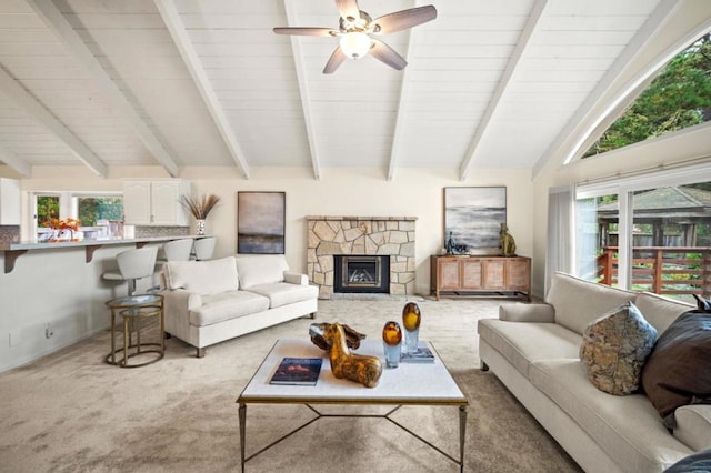 carpeted living room with lofted ceiling with beams, a stone fireplace, plenty of natural light, and ceiling fan