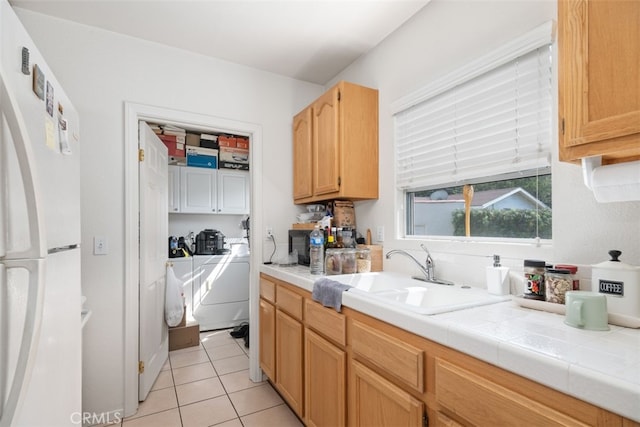 kitchen with sink, washing machine and clothes dryer, tile counters, light tile patterned floors, and white refrigerator