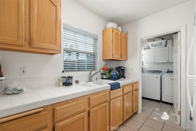 kitchen featuring light brown cabinets, light tile patterned floors, tile countertops, washing machine and clothes dryer, and sink