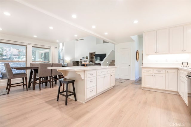 kitchen featuring white cabinetry, light hardwood / wood-style floors, a kitchen island, and a breakfast bar area