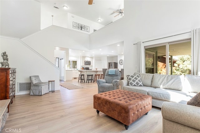 living room featuring a high ceiling, ceiling fan, and light hardwood / wood-style flooring