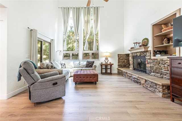 living room with light hardwood / wood-style floors, ceiling fan, and a stone fireplace