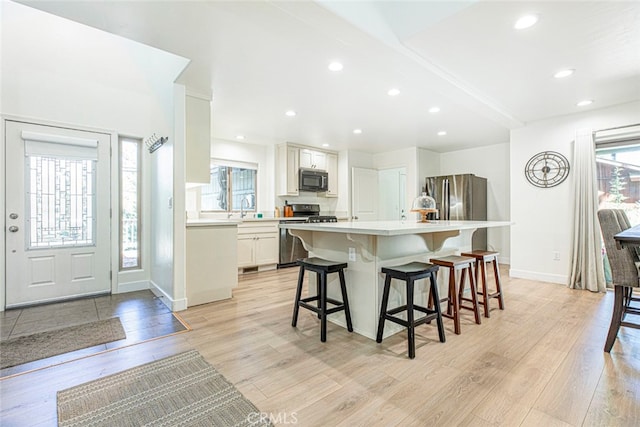 kitchen featuring light hardwood / wood-style flooring, a kitchen breakfast bar, appliances with stainless steel finishes, and white cabinetry