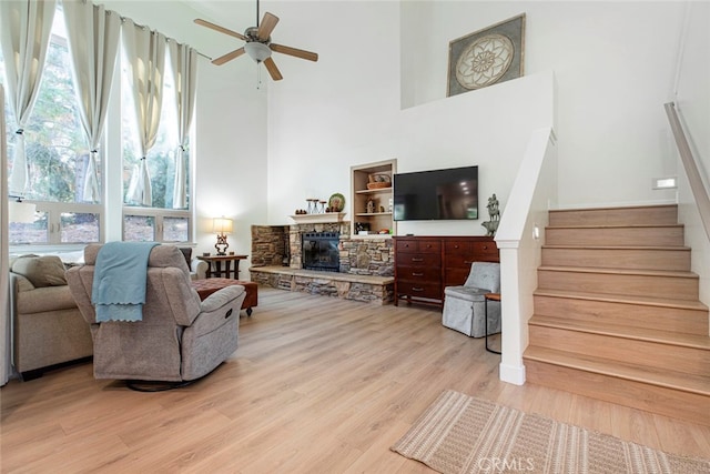 living room featuring ceiling fan, a fireplace, light wood-type flooring, and a high ceiling