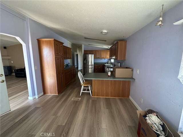 kitchen with kitchen peninsula, wood-type flooring, vaulted ceiling, appliances with stainless steel finishes, and a kitchen bar