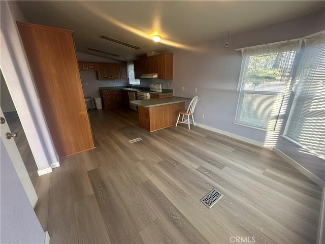 kitchen featuring a peninsula, light wood-style floors, open floor plan, white range with gas cooktop, and brown cabinetry