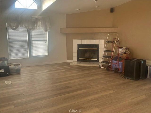 unfurnished living room featuring a tiled fireplace, wood finished floors, and baseboards