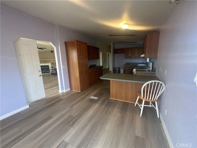 kitchen featuring brown cabinetry, light wood-style flooring, stove, a peninsula, and a fireplace