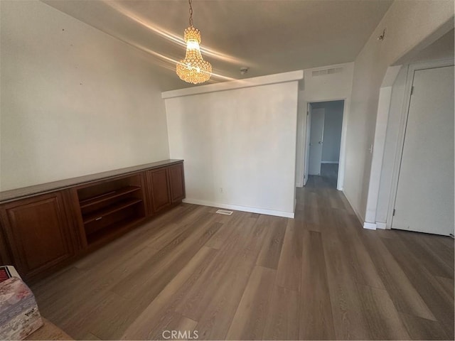 unfurnished room with an inviting chandelier, baseboards, visible vents, and wood finished floors