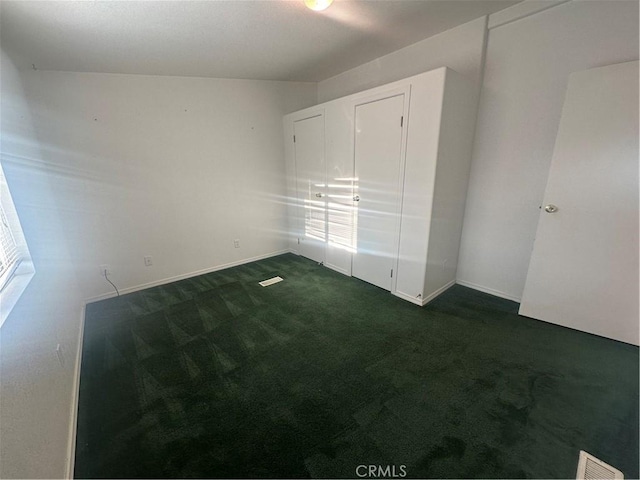 unfurnished bedroom with dark colored carpet, visible vents, and baseboards