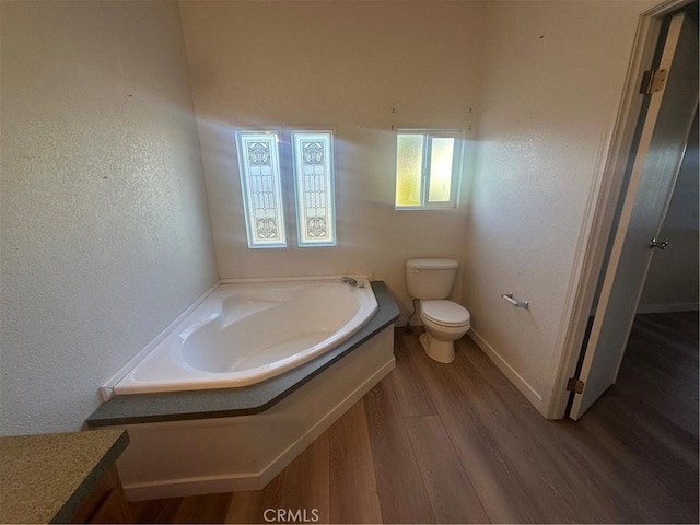 bathroom with a textured wall, toilet, wood finished floors, baseboards, and a bath