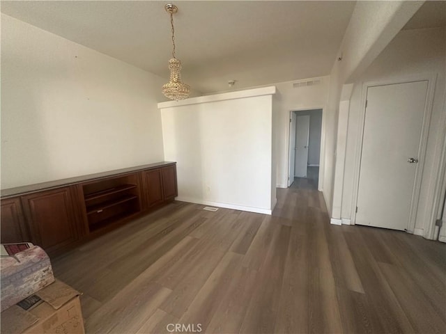 empty room featuring dark wood-style flooring, visible vents, and baseboards