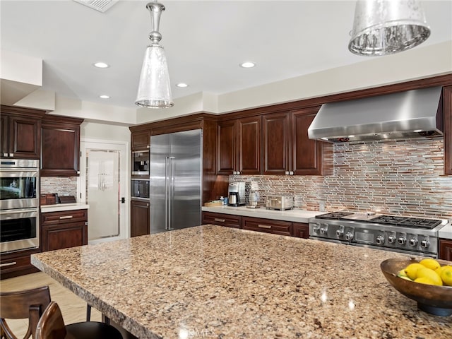 kitchen featuring a kitchen breakfast bar, decorative backsplash, wall chimney exhaust hood, high end appliances, and decorative light fixtures